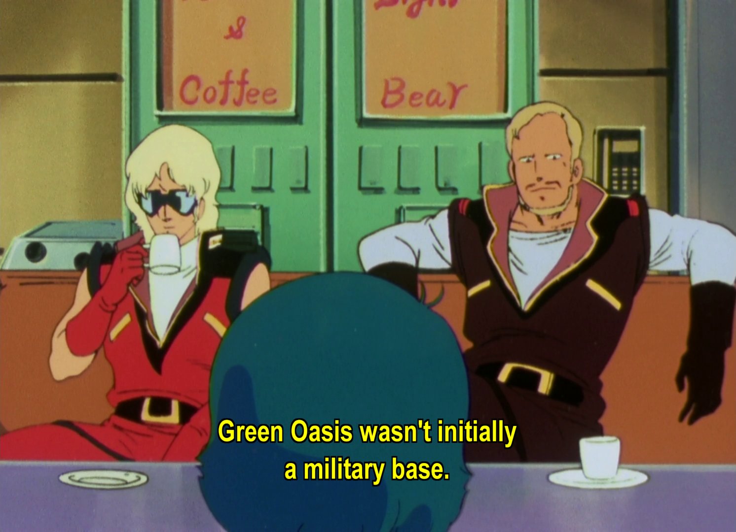 Lt Quattro Bajeena, a man who looks suspiciously like Char Aznable, and Henken, a blond man with a small beard and moustache, sitting on a couch in front of two drinks machines. The machines are labelled Coffee and Bear.