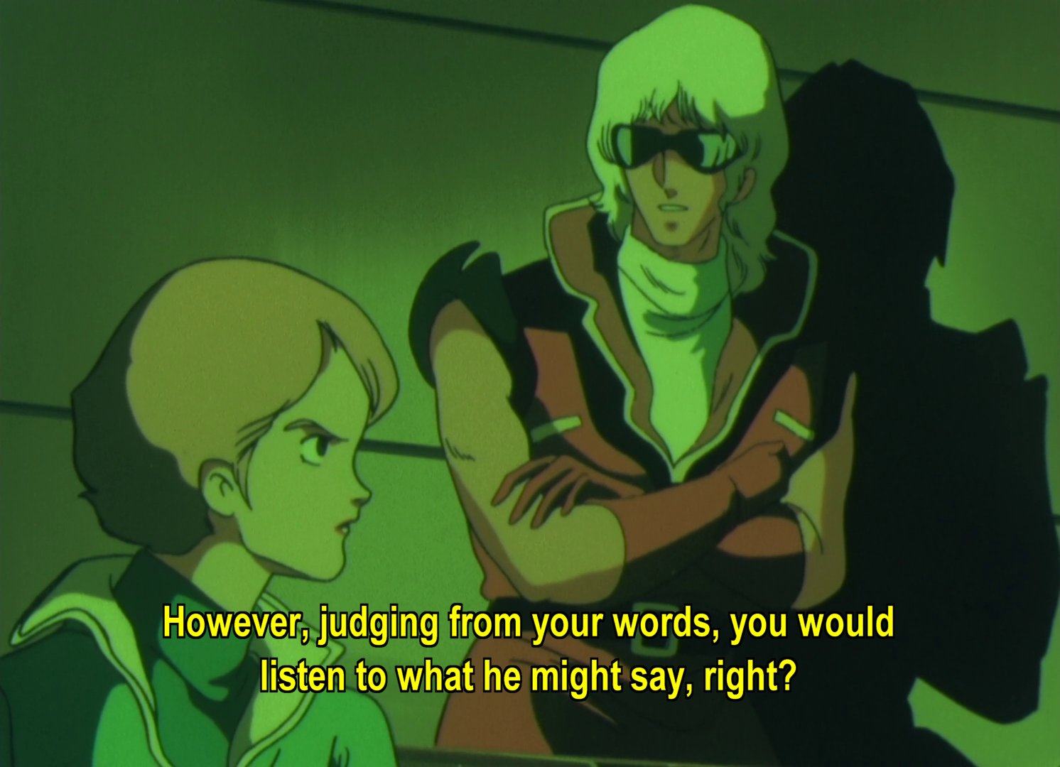 Lt Bajeena leaning against a wall, talking to Reccoa, a woman with short ginger hair.  Subtitles: However, judging from your words, you would listen to what he might say, right?