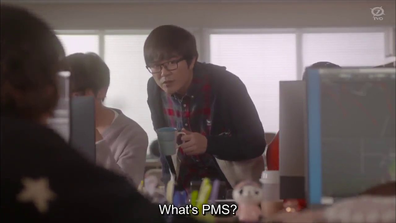 Masaru and Matsuda at their desk, with Hiyama, a man with glasses, leaning between them.  Hiyama: What's PMS?