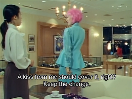 Lila, a woman with a pink bobcut and wearing a blue suit with a skirt talking to a female sales clerk.  Lila: A kiss from me should cover it, right?  Keep the change.