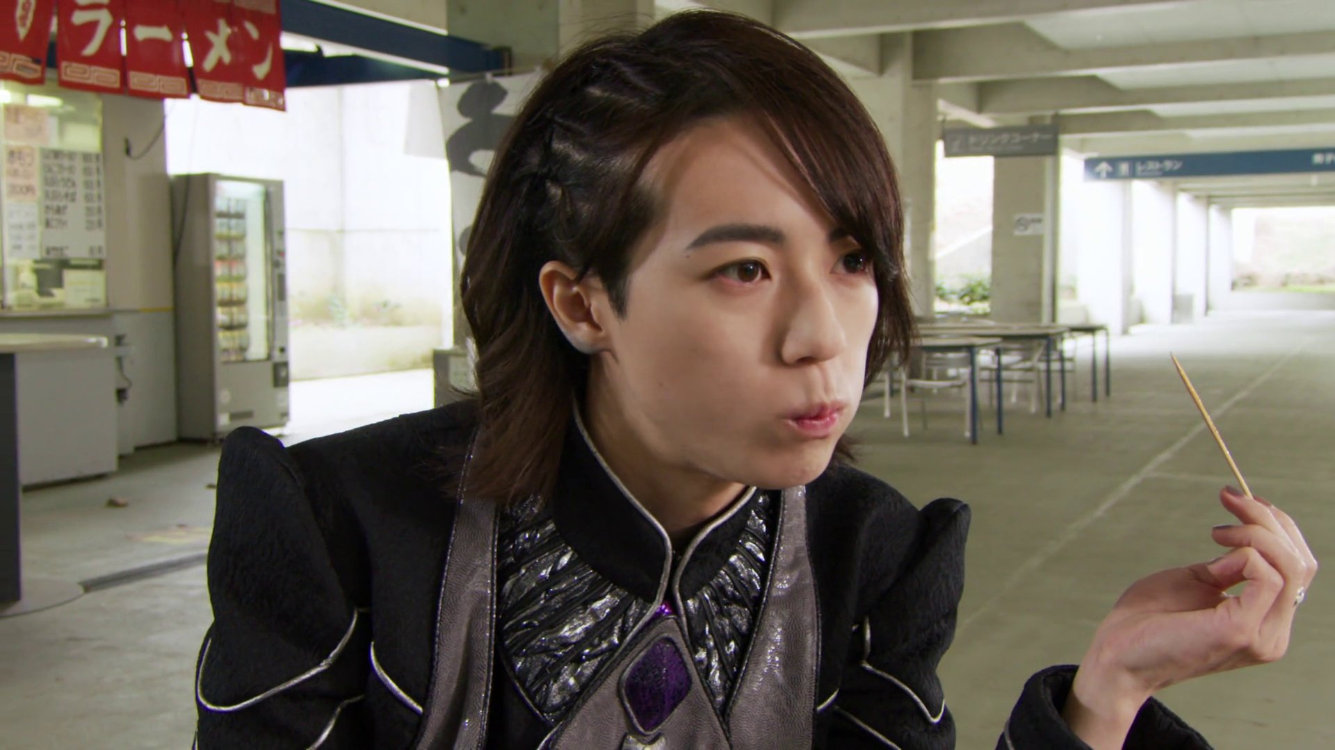 Close shot of Stacey eat takoyaki, can now see he has shoulder-length hair, with twists on one side.